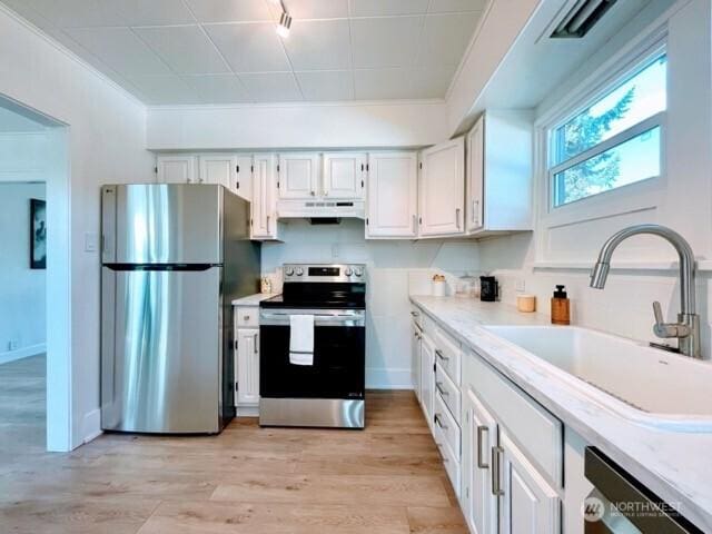 kitchen with appliances with stainless steel finishes, a sink, under cabinet range hood, light countertops, and crown molding