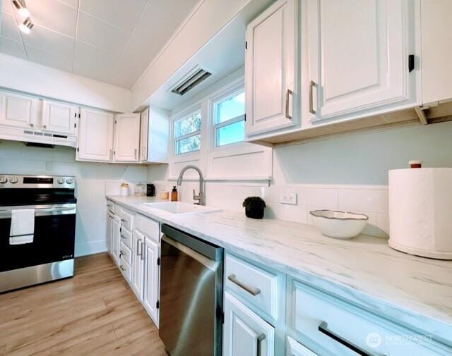 kitchen with stainless steel appliances, under cabinet range hood, a sink, white cabinetry, and light wood-style flooring