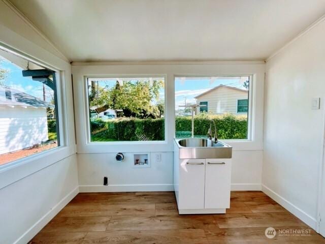 doorway to outside featuring a sink, light wood-style floors, lofted ceiling, and baseboards