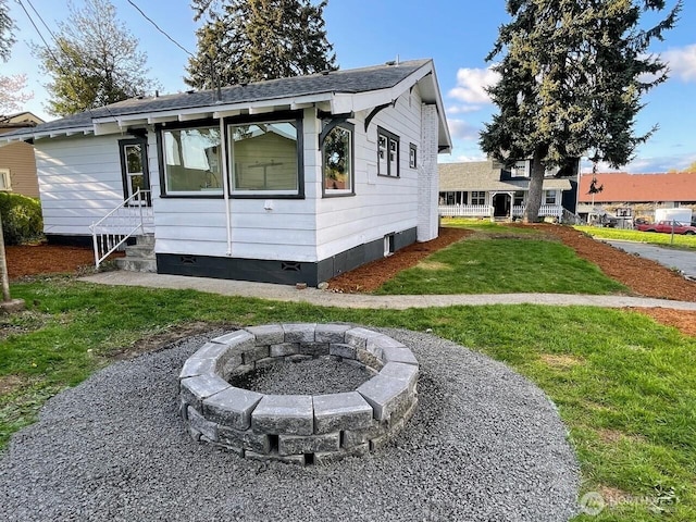 view of front of property featuring entry steps, a front yard, a fire pit, and a shingled roof