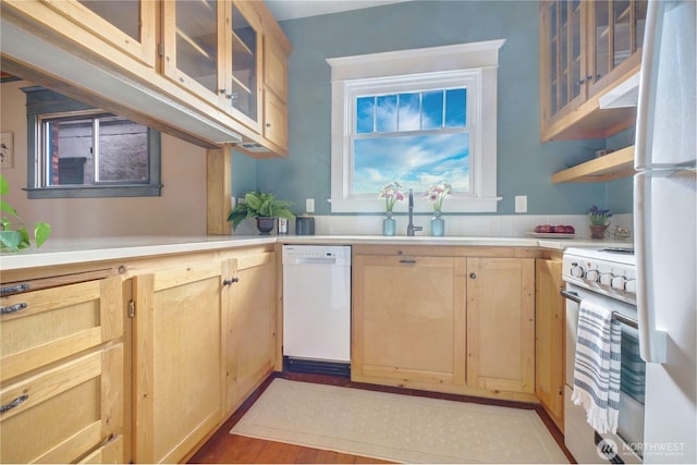 kitchen featuring white appliances, light brown cabinetry, light countertops, a sink, and glass insert cabinets