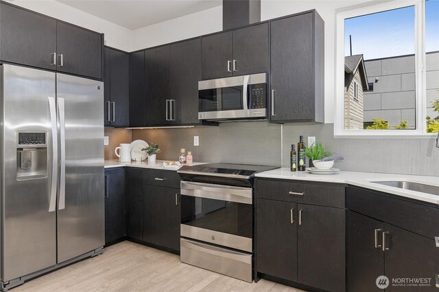 kitchen with stainless steel appliances, light countertops, light wood-style flooring, and backsplash