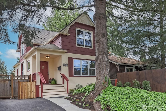 view of front of house featuring stucco siding, a shingled roof, fence, and a gate