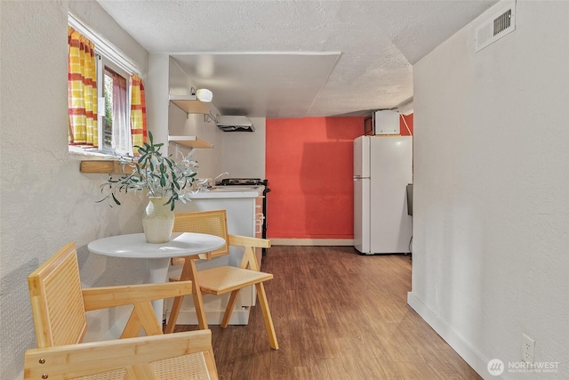 dining room featuring wood finished floors, baseboards, a textured ceiling, a wall unit AC, and a textured wall