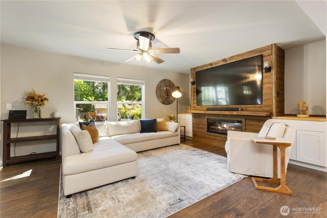 living area featuring wood finished floors, a ceiling fan, and a large fireplace