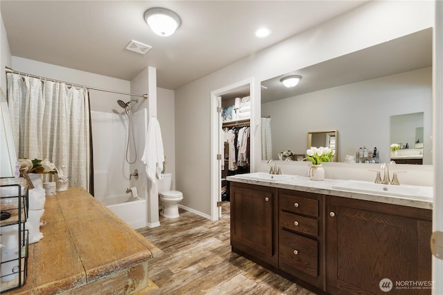 bathroom featuring wood finished floors, double vanity, shower / tub combo with curtain, toilet, and baseboards