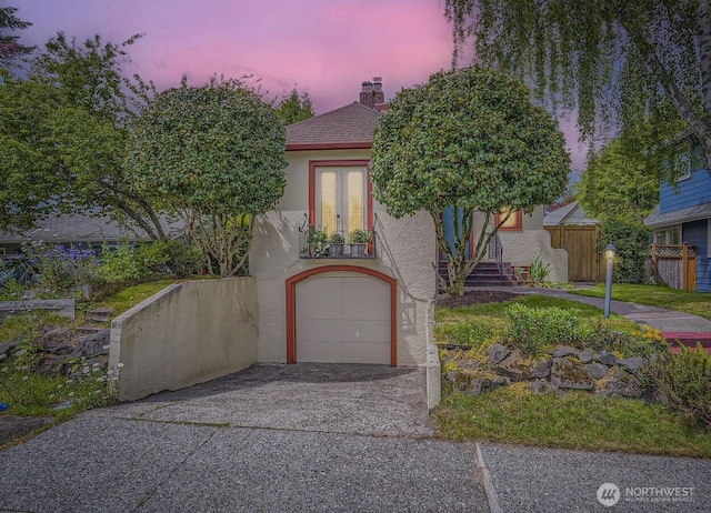 2523 Royal Ct E, Seattle, WA 98112 - view of property hidden behind natural elements featuring an attached garage, stucco siding, a chimney, and driveway