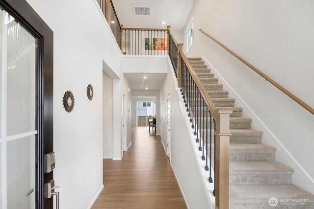 foyer featuring wood finished floors, visible vents, baseboards, a towering ceiling, and stairs