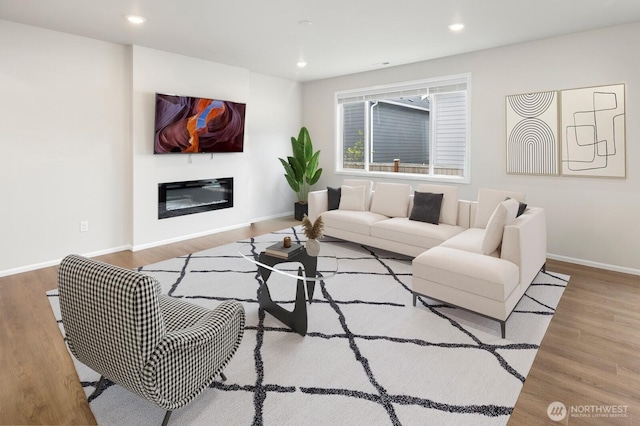 living area with recessed lighting, baseboards, a glass covered fireplace, and wood finished floors