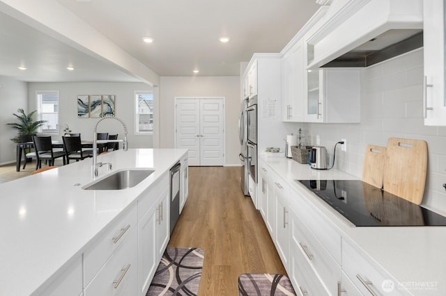 kitchen with a sink, tasteful backsplash, light countertops, black electric cooktop, and custom range hood