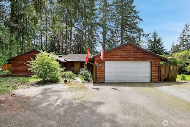 view of front facade with an attached garage, asphalt driveway, and fence