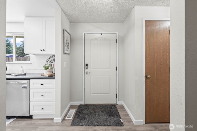 doorway featuring baseboards, light wood-style flooring, visible vents, and a textured ceiling