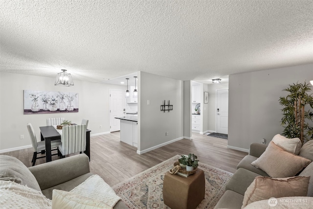 living room featuring radiator, a textured ceiling, baseboards, light wood-style flooring, and a notable chandelier