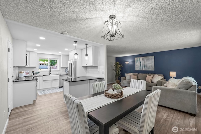 dining space featuring an inviting chandelier, a textured ceiling, light wood-type flooring, and recessed lighting