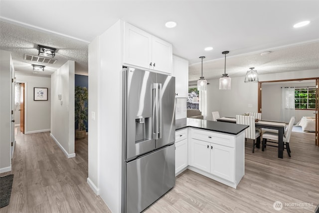 kitchen featuring visible vents, a peninsula, stainless steel fridge, dark countertops, and white cabinets