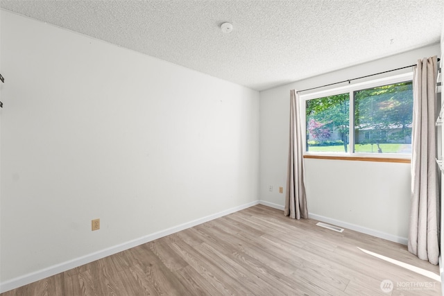 spare room with baseboards, light wood-style floors, visible vents, and a textured ceiling