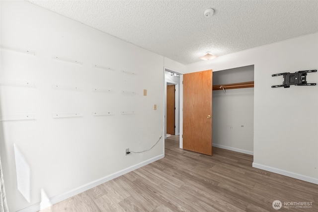 unfurnished bedroom featuring a textured ceiling, a closet, baseboards, and light wood-style floors