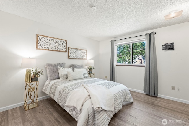 bedroom with a textured ceiling, wood finished floors, and baseboards