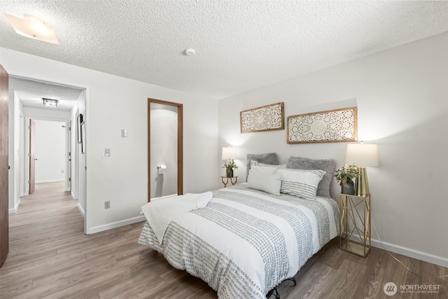 bedroom featuring baseboards, a textured ceiling, and wood finished floors