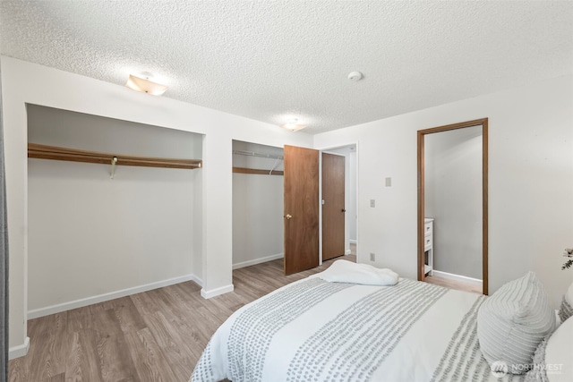 bedroom with light wood finished floors, a textured ceiling, baseboards, and multiple closets