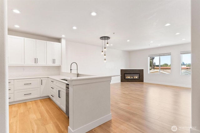 kitchen with a sink, light wood finished floors, recessed lighting, a peninsula, and white cabinets