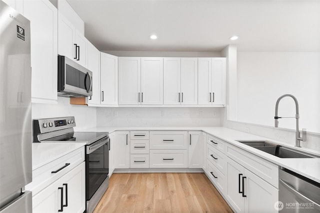 kitchen featuring appliances with stainless steel finishes, a sink, white cabinets, light wood-style flooring, and light countertops