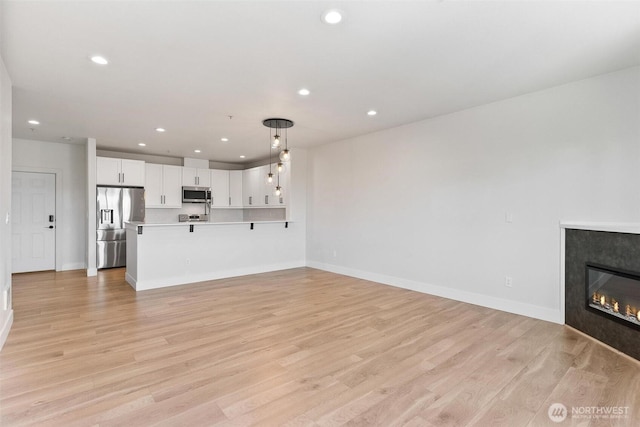 unfurnished living room featuring recessed lighting, light wood finished floors, baseboards, and a glass covered fireplace