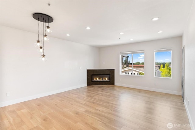 unfurnished living room featuring light wood finished floors, a glass covered fireplace, recessed lighting, and baseboards