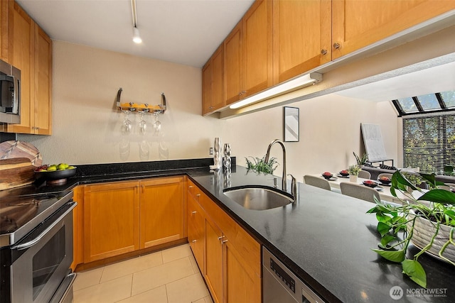 kitchen featuring appliances with stainless steel finishes, a sink, light tile patterned floors, and brown cabinetry