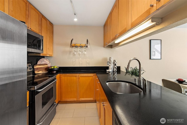 kitchen with appliances with stainless steel finishes, a sink, light tile patterned flooring, dark countertops, and brown cabinets