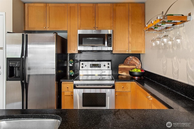 kitchen with stainless steel appliances, dark stone counters, and brown cabinetry