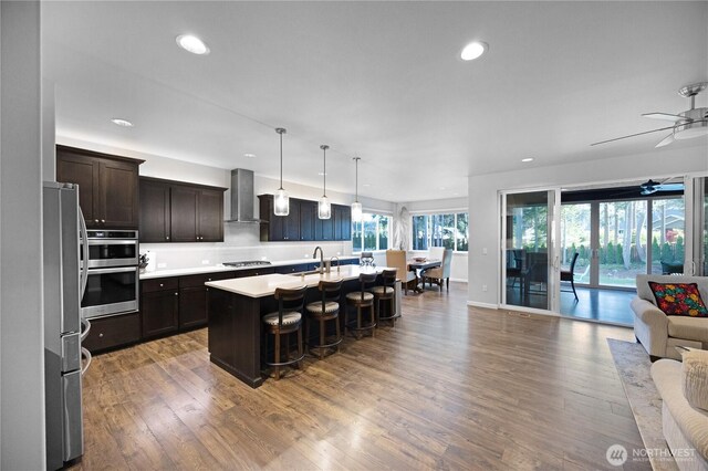 kitchen featuring open floor plan, appliances with stainless steel finishes, wall chimney range hood, recessed lighting, and a kitchen bar