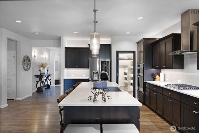 kitchen featuring appliances with stainless steel finishes, a sink, wall chimney range hood, light countertops, and recessed lighting