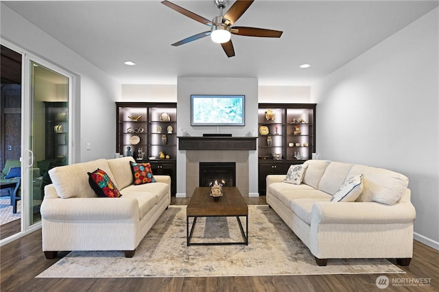 living area with wood finished floors, ceiling fan, a tiled fireplace, recessed lighting, and baseboards