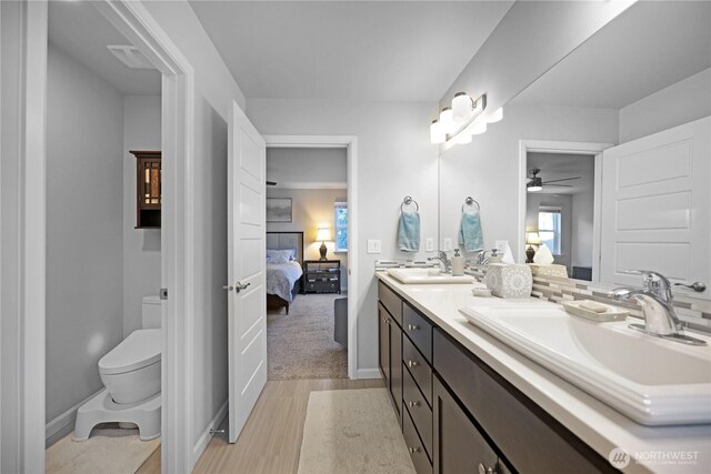 full bath with connected bathroom, toilet, ceiling fan, wood finished floors, and double vanity