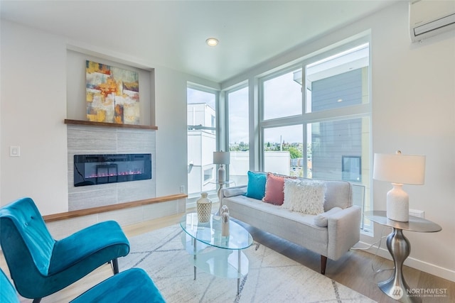 living room with wood finished floors, a wall mounted air conditioner, baseboards, a glass covered fireplace, and recessed lighting
