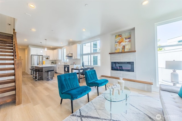 living room with recessed lighting, light wood-style floors, stairway, and a glass covered fireplace