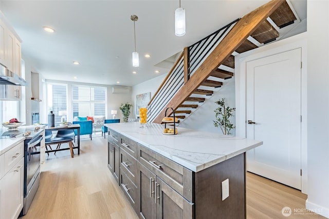 kitchen featuring light wood finished floors, stainless steel electric range, white cabinetry, decorative light fixtures, and a kitchen island