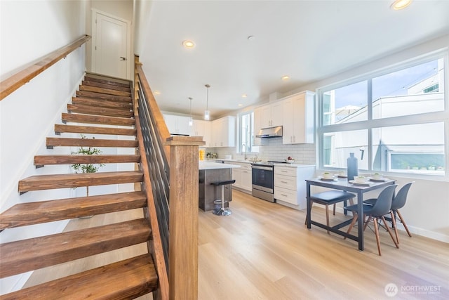 kitchen with a sink, stainless steel electric range, white cabinetry, under cabinet range hood, and light countertops