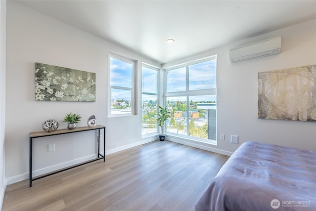 bedroom featuring baseboards, multiple windows, a wall mounted air conditioner, and wood finished floors