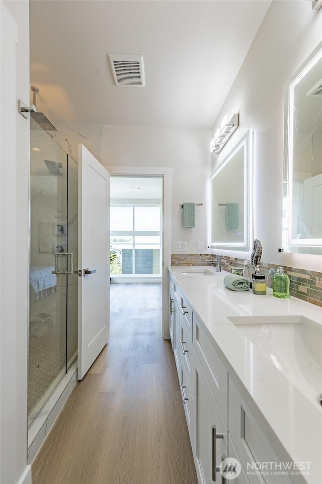 bathroom featuring visible vents, a sink, double vanity, wood finished floors, and a marble finish shower