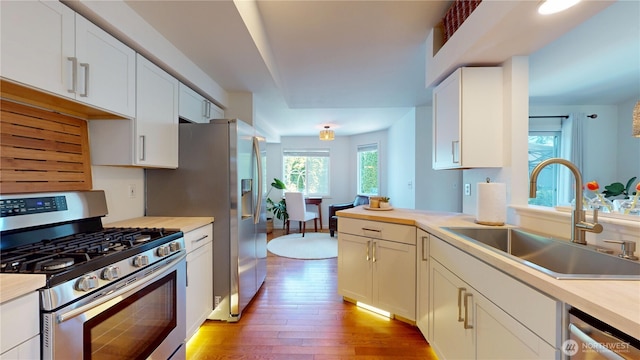 kitchen with a sink, white cabinetry, light wood-style floors, light countertops, and appliances with stainless steel finishes