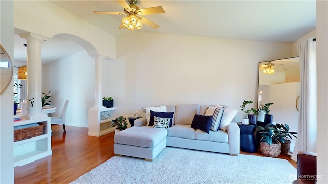 living area featuring ornate columns, wood finished floors, ceiling fan, arched walkways, and vaulted ceiling