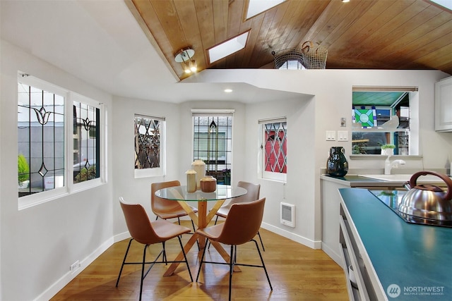 dining room featuring wooden ceiling, lofted ceiling, a skylight, baseboards, and light wood-style flooring
