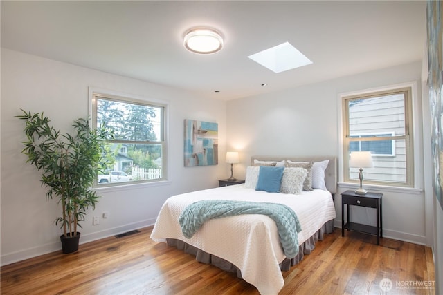 bedroom with a skylight, wood finished floors, and baseboards