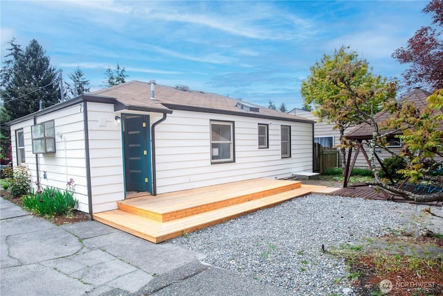 back of house featuring fence, a wooden deck, and a shingled roof
