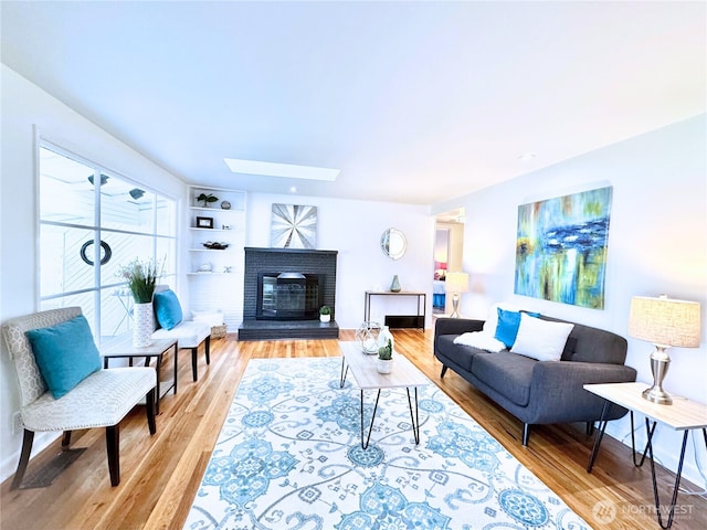 living room with a fireplace, light wood-style flooring, and a skylight