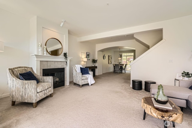 living area featuring arched walkways, light carpet, a tile fireplace, and baseboards
