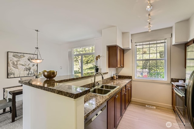 kitchen featuring stainless steel dishwasher, a sink, a peninsula, brown cabinets, and baseboards
