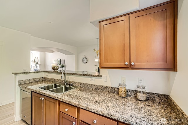 kitchen featuring a sink, dishwasher, stone countertops, arched walkways, and brown cabinetry